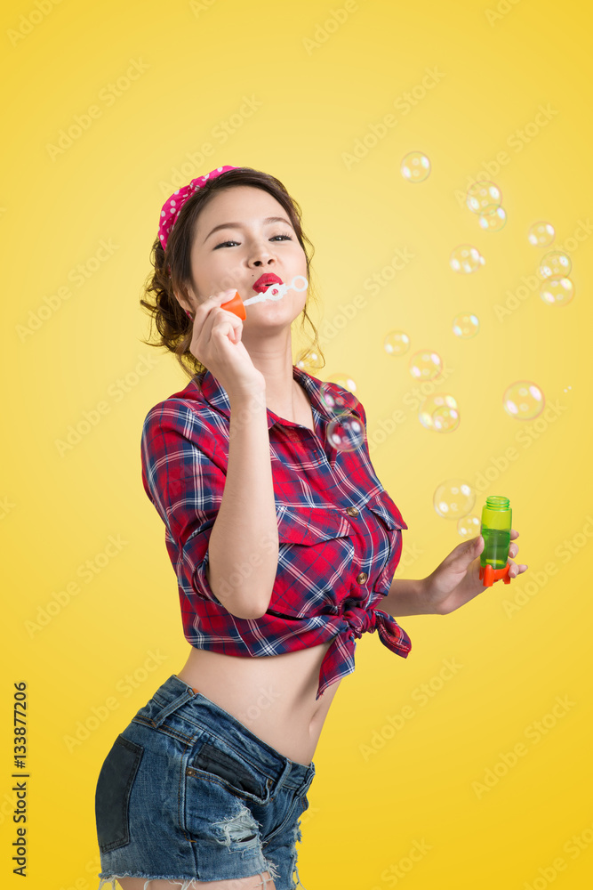 Pinup model blowing soap bubbles over yellow background.