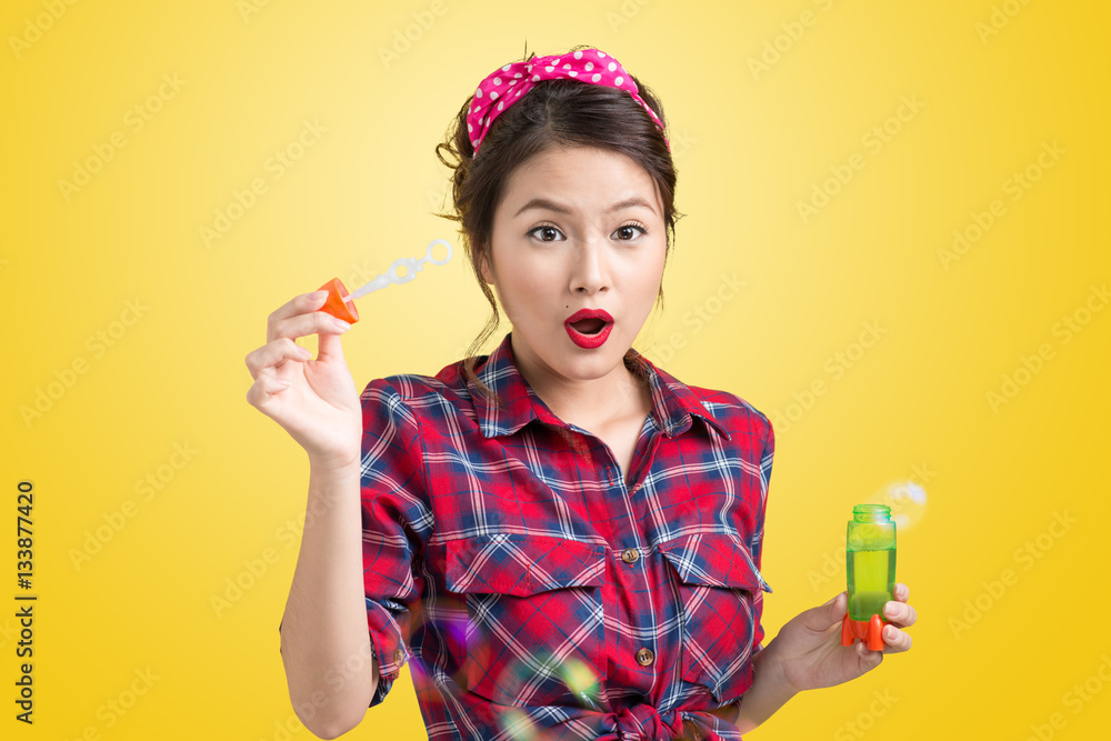 Pinup model blowing soap bubbles over yellow background.