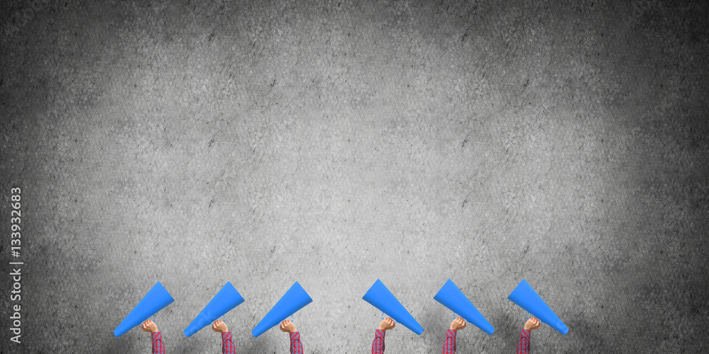 Many hands of woman holding paper trumpet against concrete background