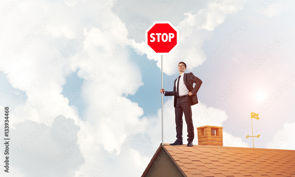 Caucasian businessman on brick house roof showing stop road sign