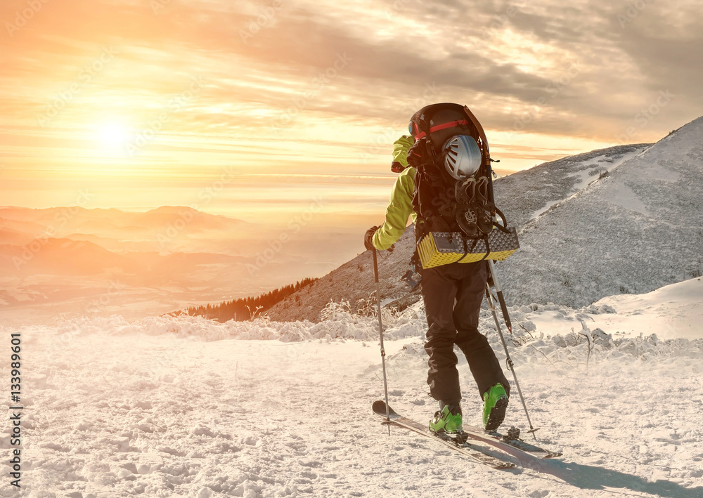 Men with backpack at ski goes to the top of mountain in sun day