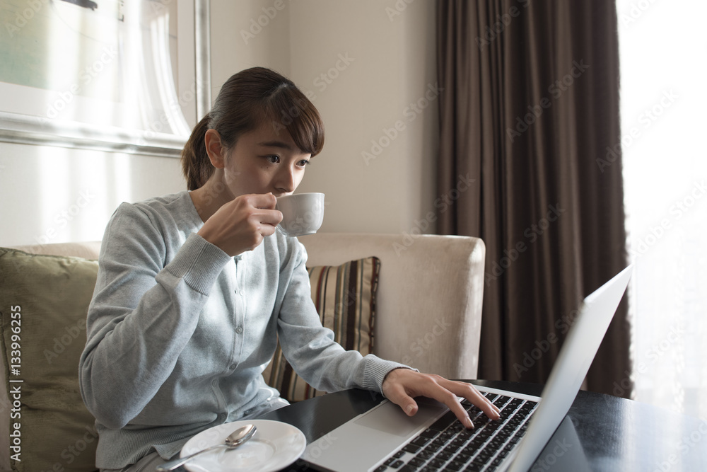 A woman is working on a laptop while drinking coffee