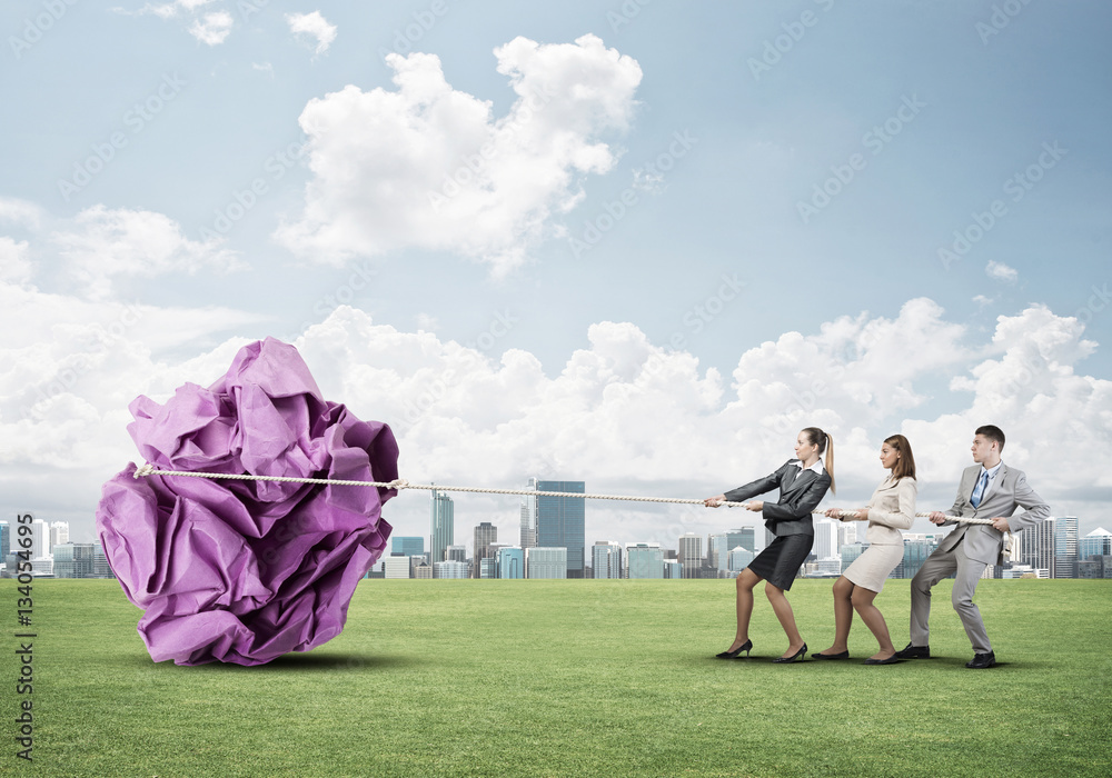 Young business people outdoors and huge paper ball as symbol of creativity