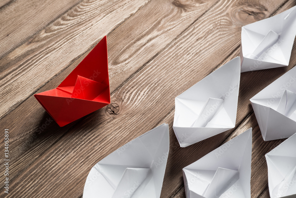 Business leadership concept with white and color paper boats on wooden table