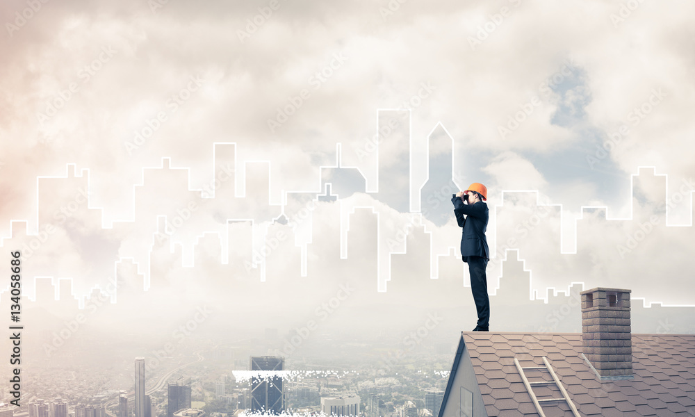 Engineer man standing on roof and looking in binoculars. Mixed m