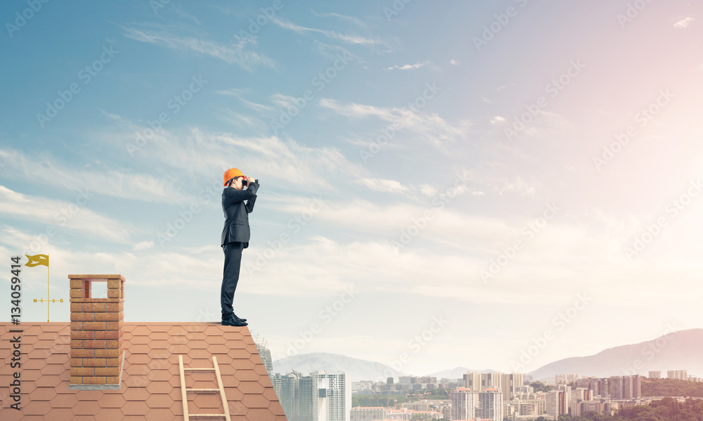 Engineer man standing on roof and looking in binoculars. Mixed m