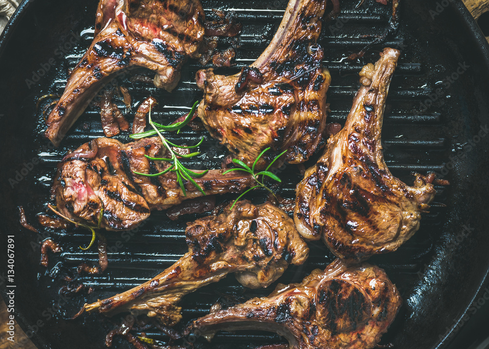 Barbecue dinner. Grilled lamb meat chops with onion and rosemary in black cast iron pan, top view, c