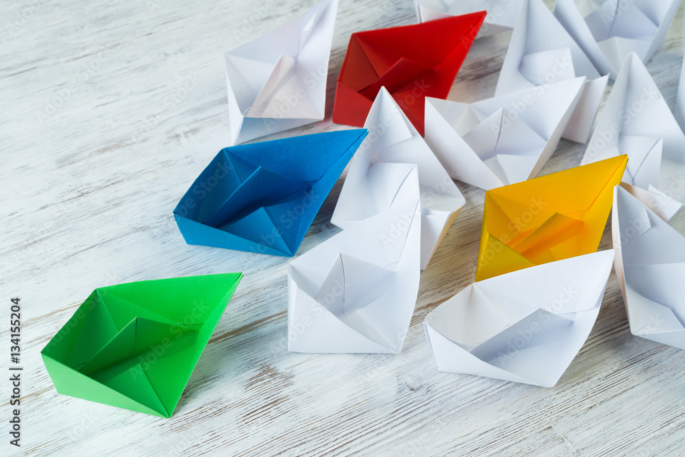 Business leadership concept with white and color paper boats on wooden table