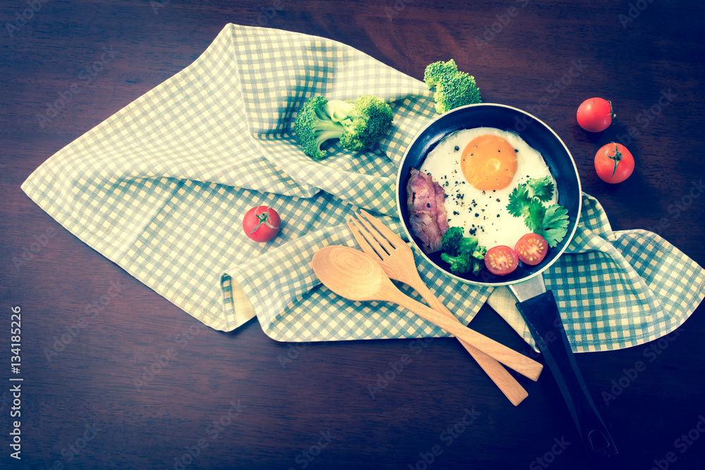 Breakfast with fried egg and bacon in dark pan on the table