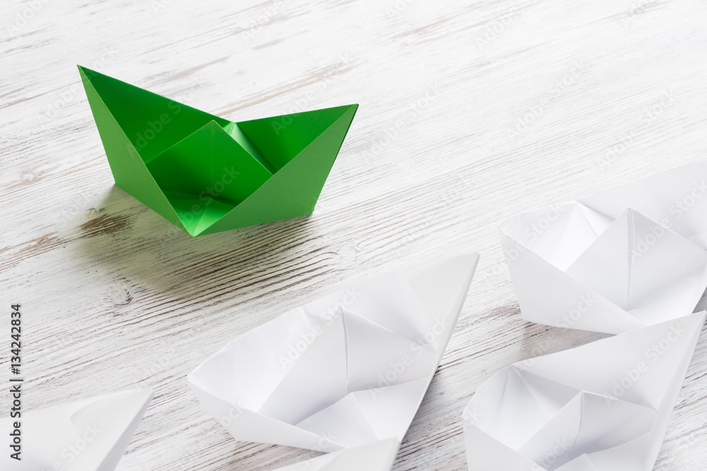 Business leadership concept with white and color paper boats on wooden table