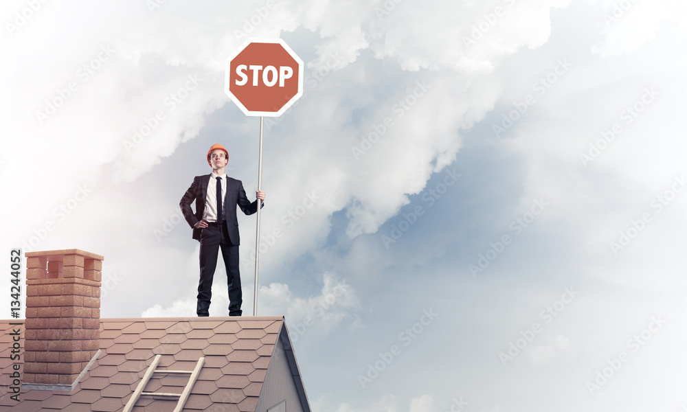 Caucasian businessman on brick house roof showing stop road sign