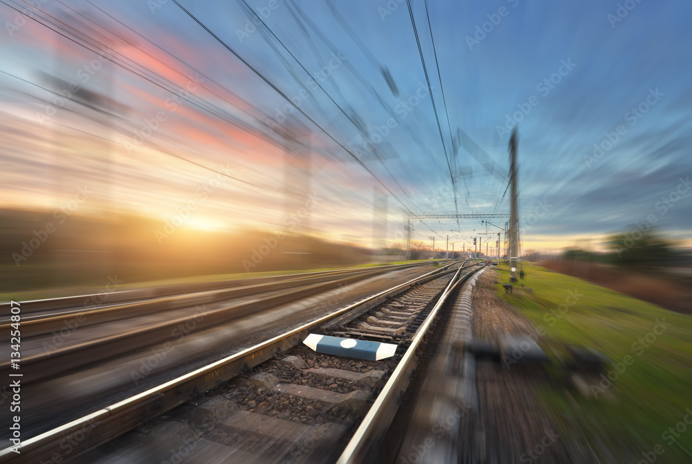 Railroad in motion at sunset. Railway station with motion blur effect against colorful sunny sky, In