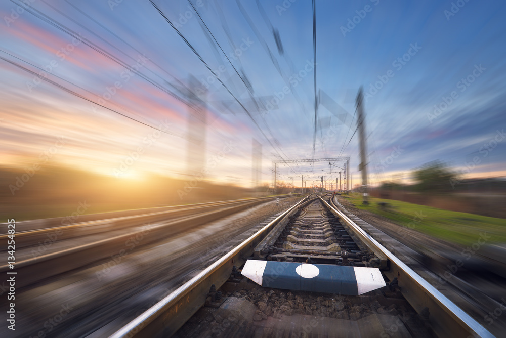 Railroad in motion at sunset. Railway station with motion blur effect against colorful sunny sky, In