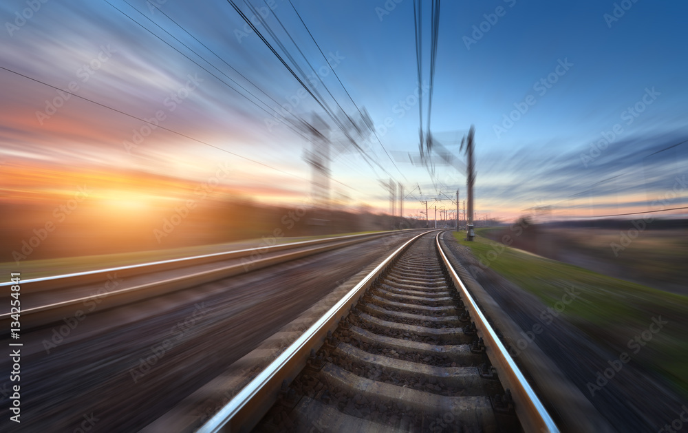 Railroad in motion at sunset. Railway station with motion blur effect against colorful blue sky, Ind