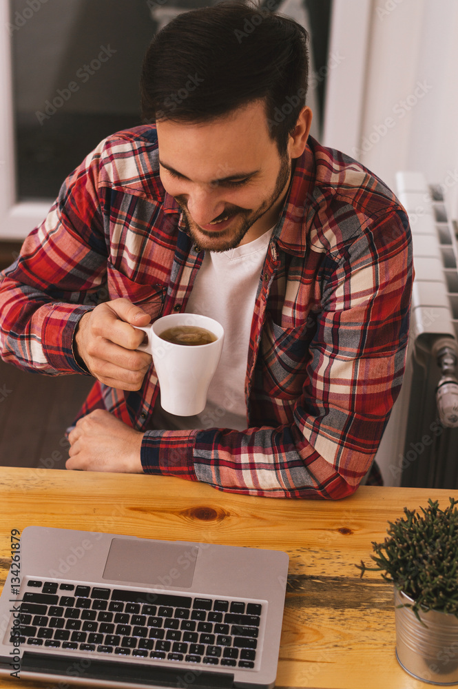 Young handsome man drinking tea and looking at laptop screen