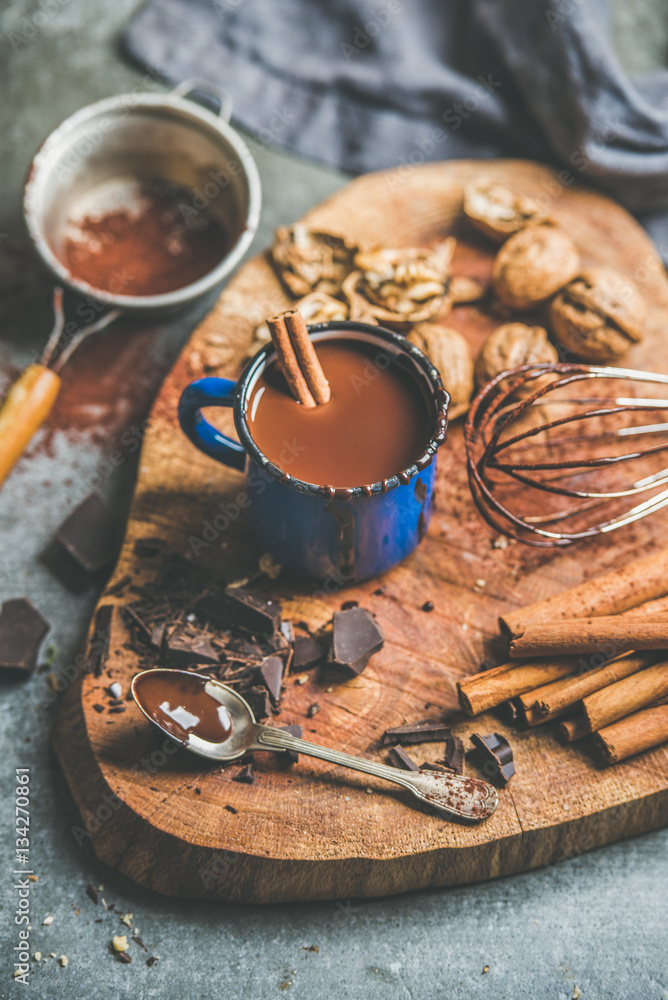 Making rich winter hot chocolate with cinnamon sticks and walnuts in blue enamel mug on wooden board