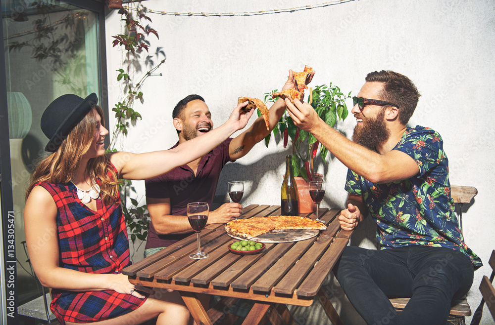 Friends toast with pizza and laugh while outside