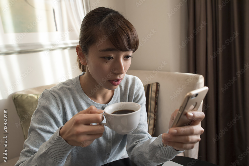 A woman is watching a cell phone while drinking coffee