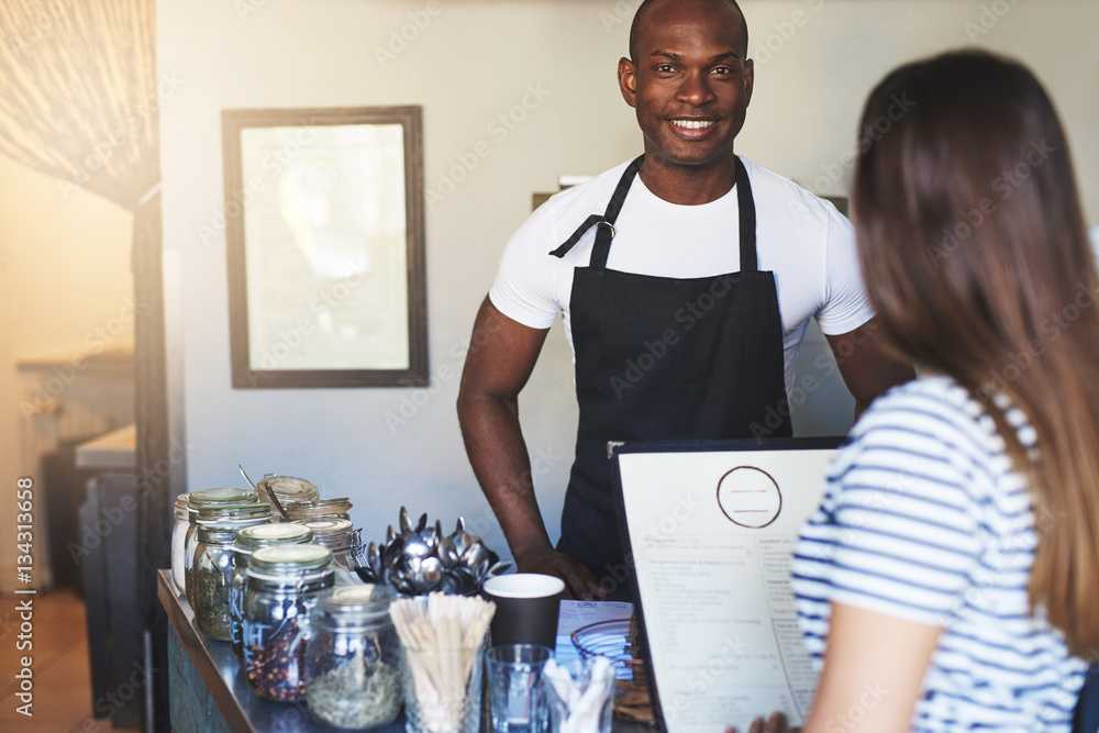 Black smiling cafe worker talking to customer