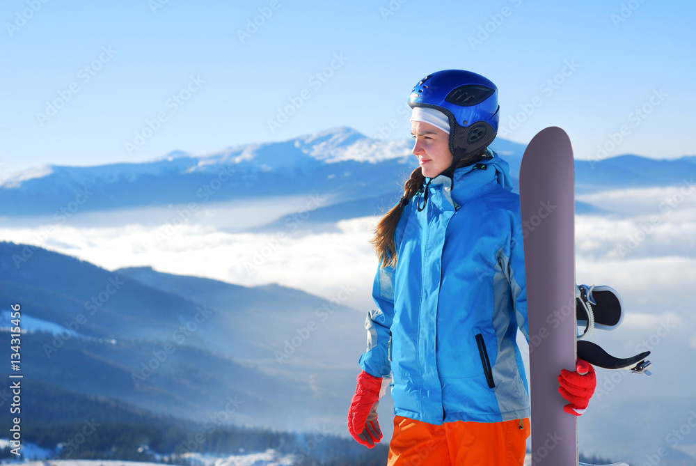 girl standing on a mountain top with snowboard in the hands