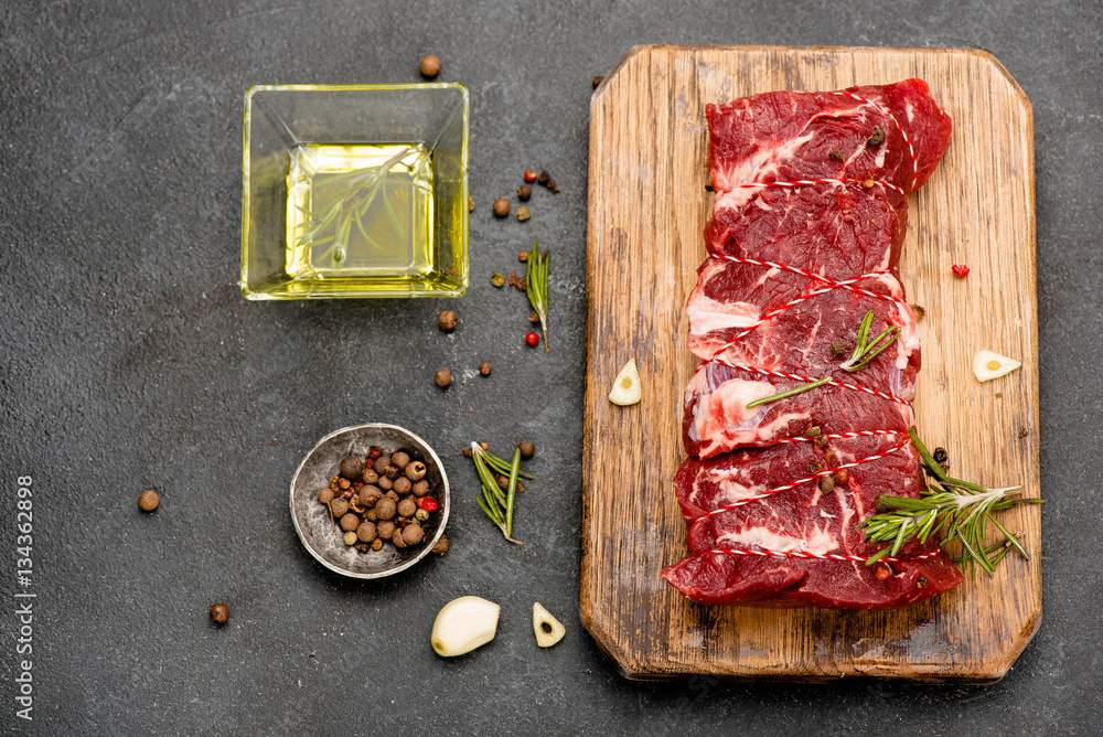 Raw meat with olive oil, spices and rosemary on wooden board. Fresh beef. Ready to roasting. Top vie