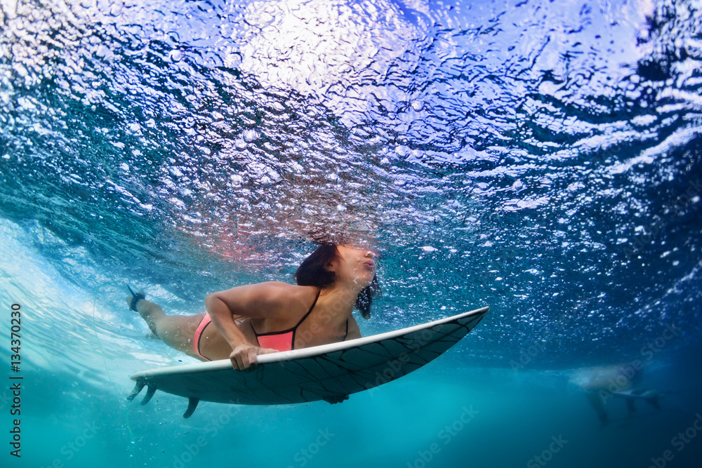 Active girl in bikini in action. Surfer woman with surf board dive underwater under breaking big wav