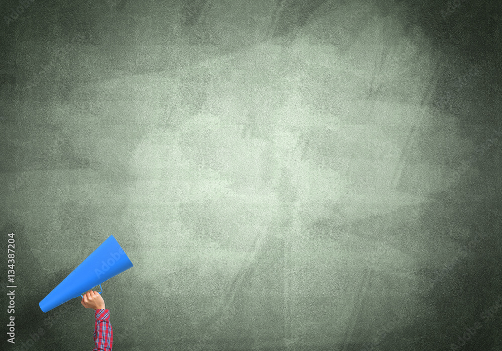 Hand of woman holding paper trumpet against concrete background