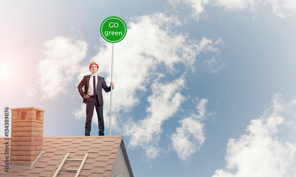 Businessman in suit on house top with ecology concept signboard.