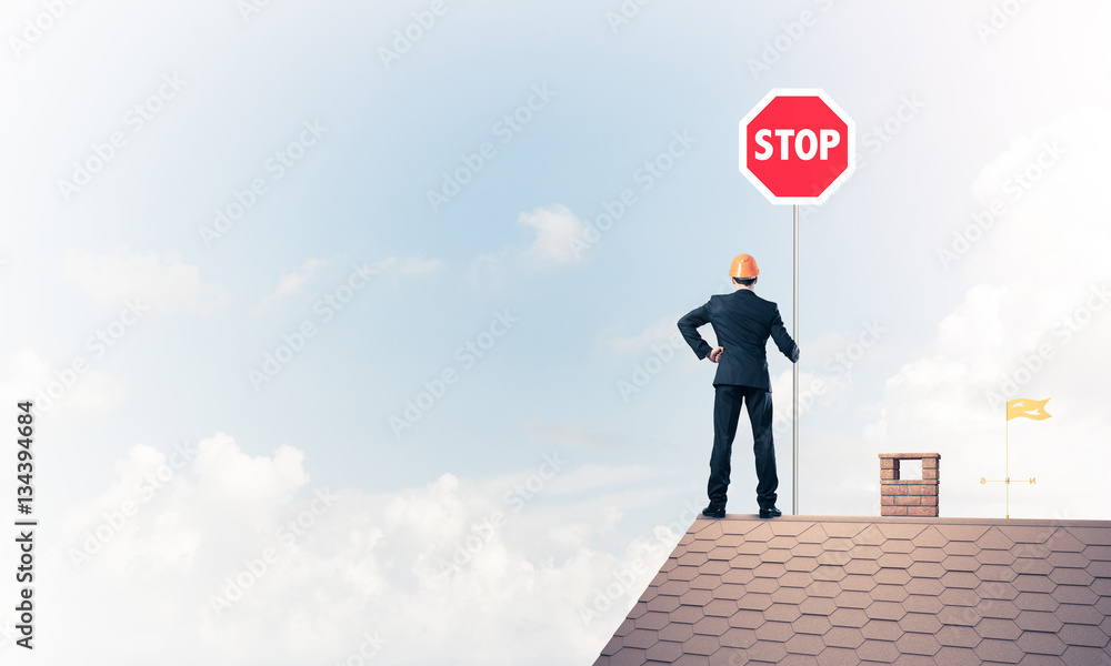 Caucasian businessman on brick house roof showing stop road sign