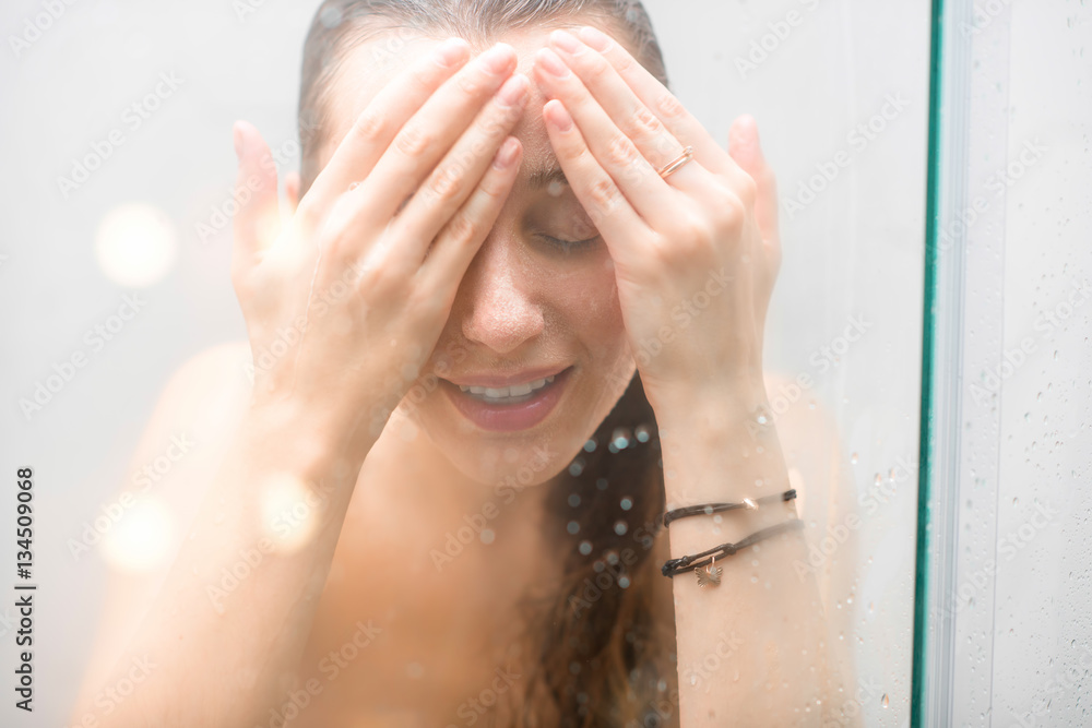 Portrait of a woman with headache standing behind the glass door in the shower