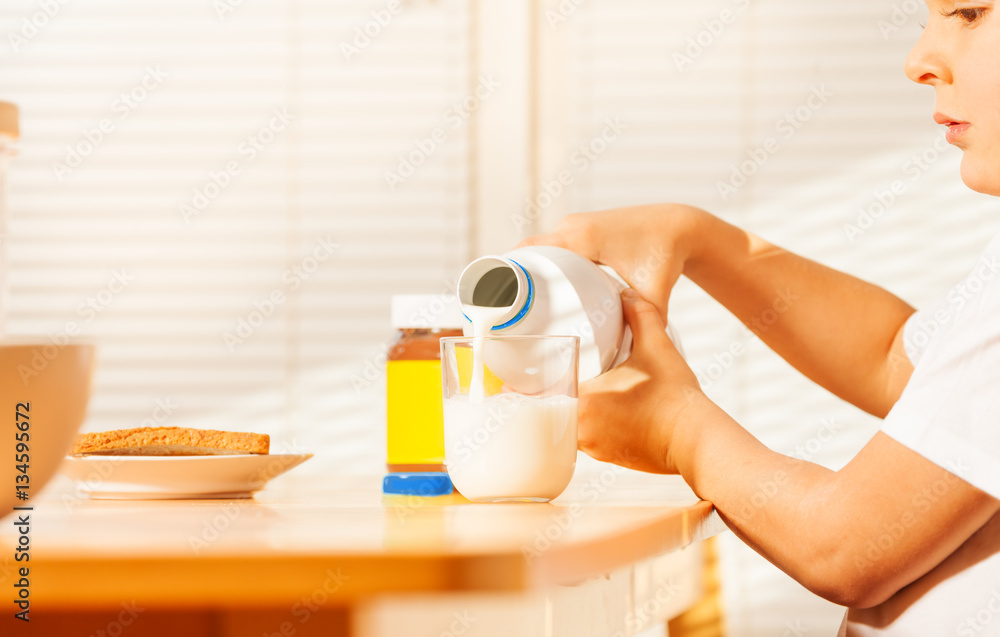 Little boy pouring milk in glass during breakfast