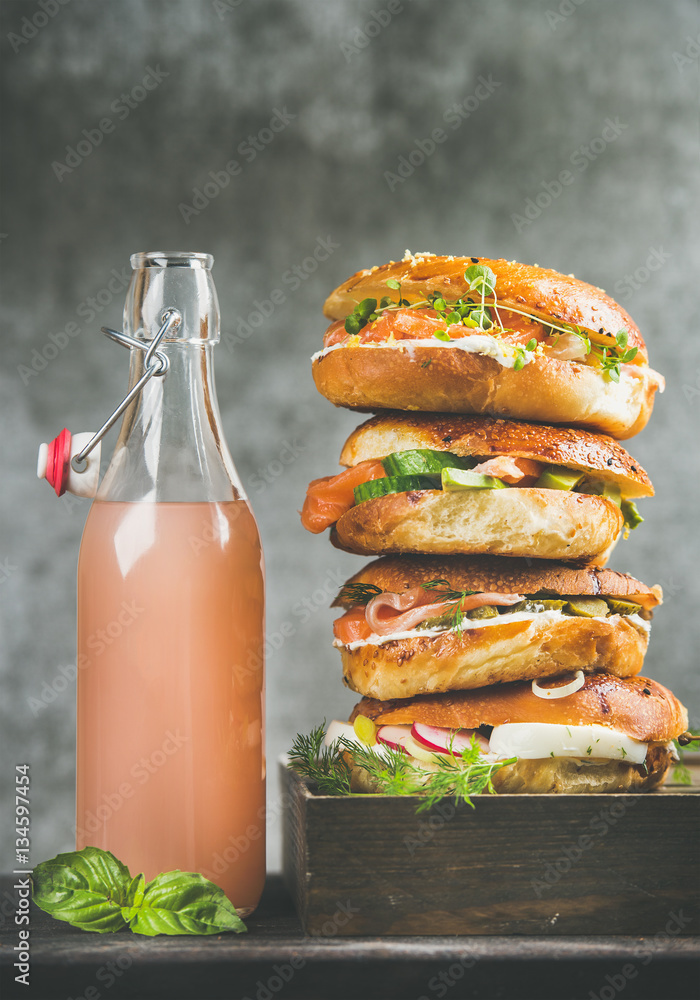 Heap of bagels with salmon, eggs, vegetables, capers and cream-cheese and bottle of grapefruit lemon