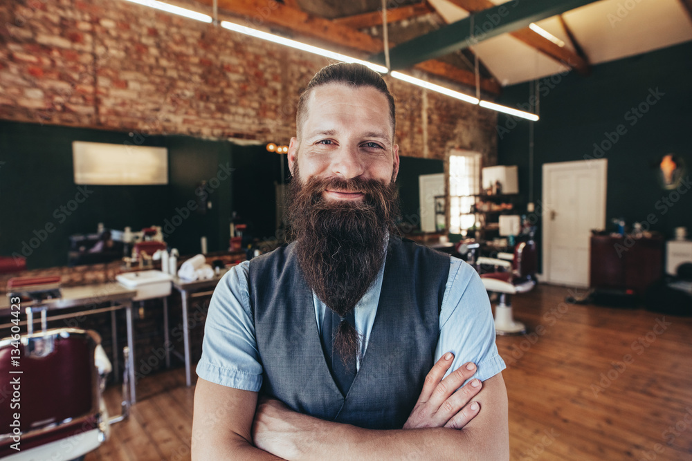 Happy young barber smiling at his barbershop