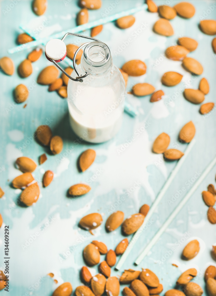 Dairy alternative milk. Almond milk in bottle and fresh nuts over blue background, selective focus, 