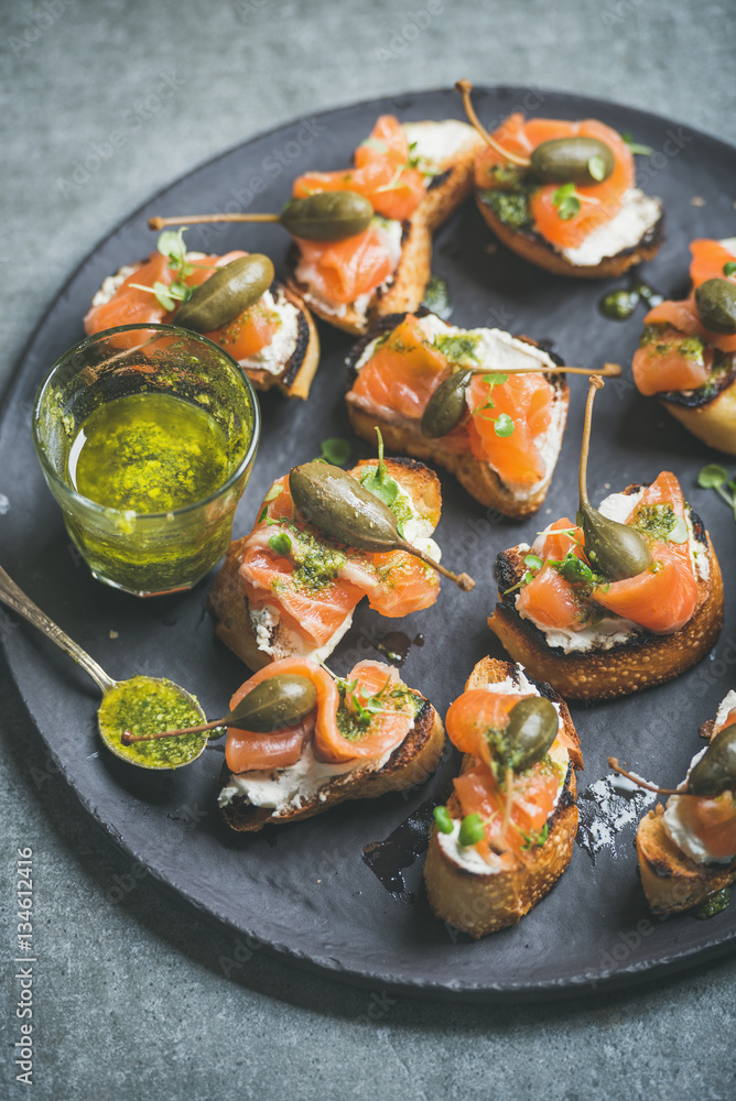 Homemade salmon crostini with cream-cheese, watercress, capers and pesto suace in round black slate 