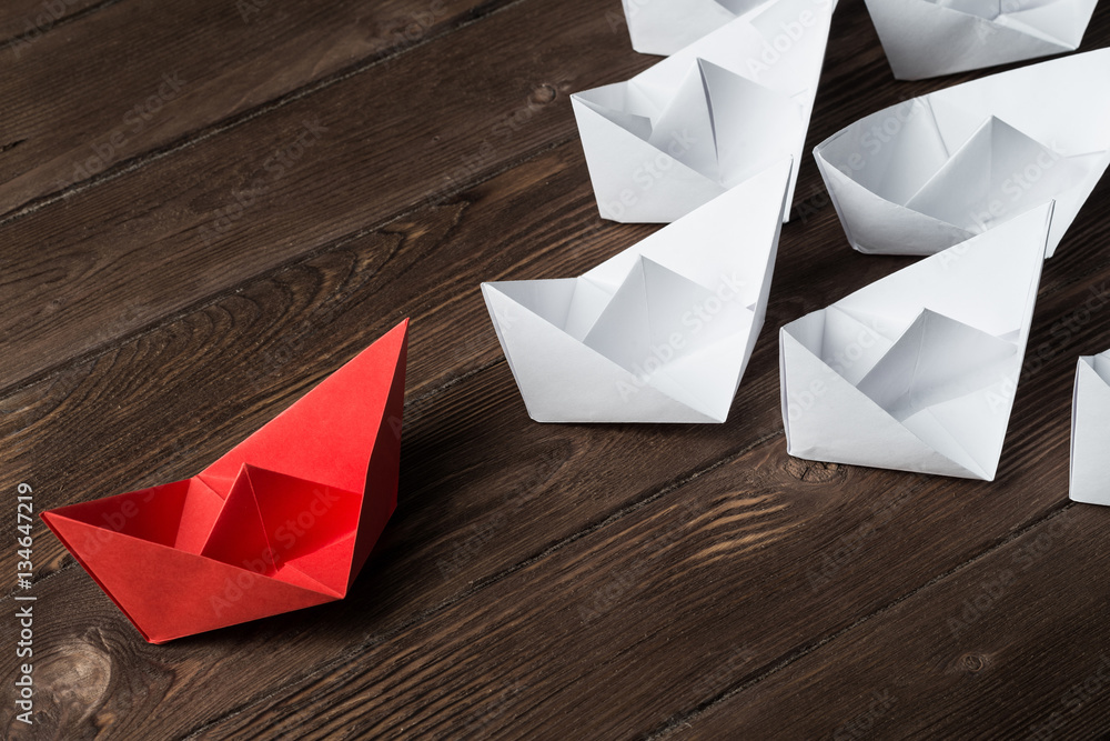 Business leadership concept with white and color paper boats on wooden table