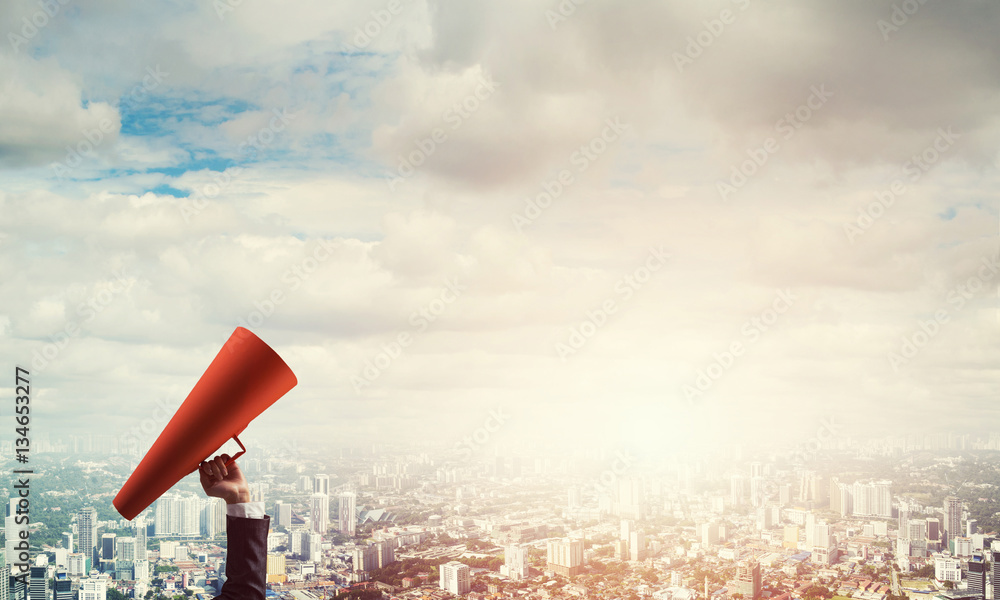 Hand of businesswoman holding red paper trumpet against cityscape background