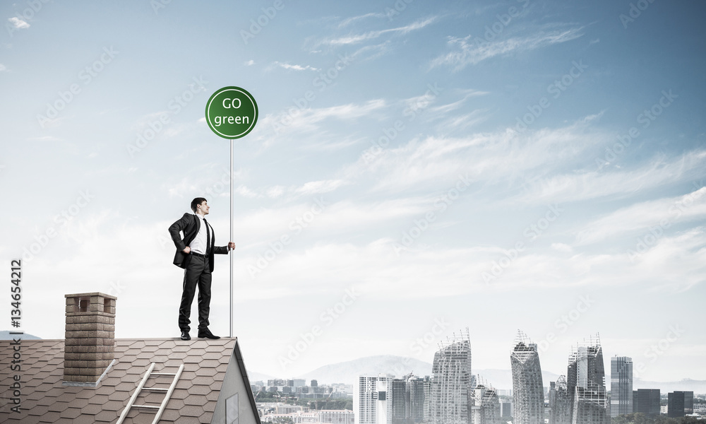 Businessman in suit on house top with ecology concept signboard.