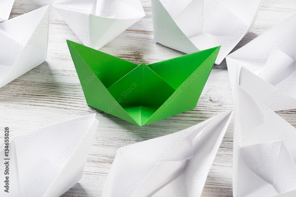 Business leadership concept with white and color paper boats on wooden table