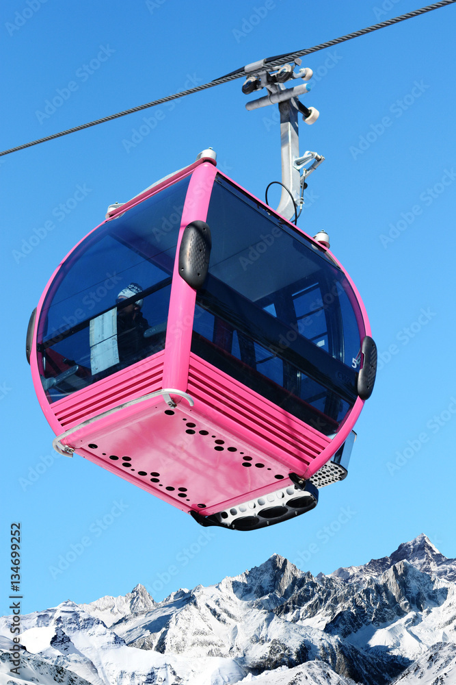 Pink cable car cabin over the snow mountain peak 