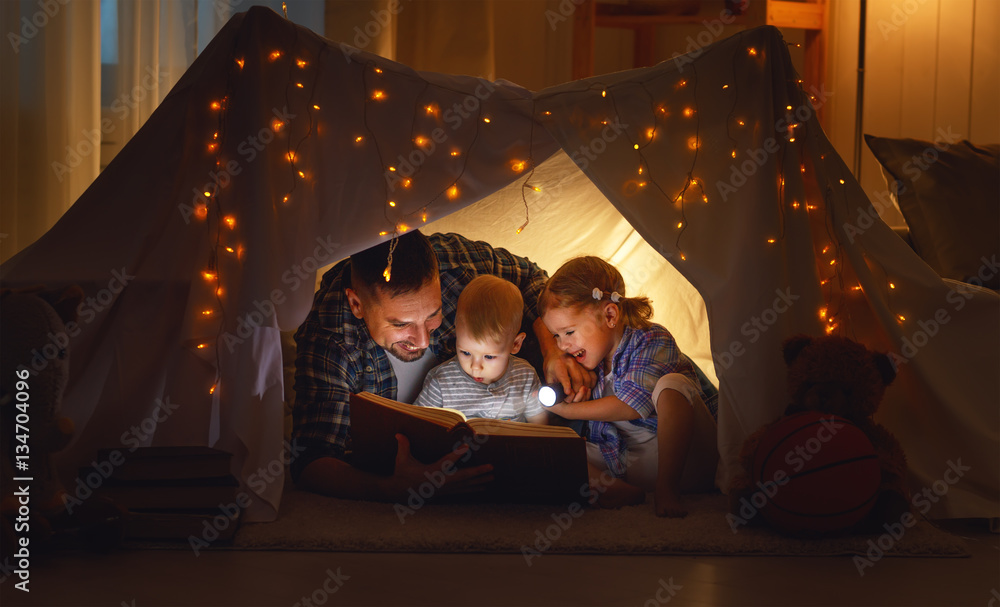 happy family father and children reading a book  in  tent at hom