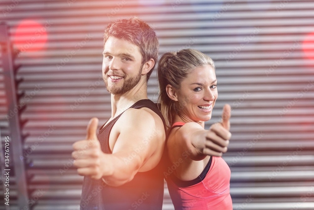 Portrait of serious couple standing back to back with thumbs up