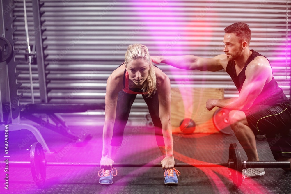 Trainer helping woman with lifting barbell