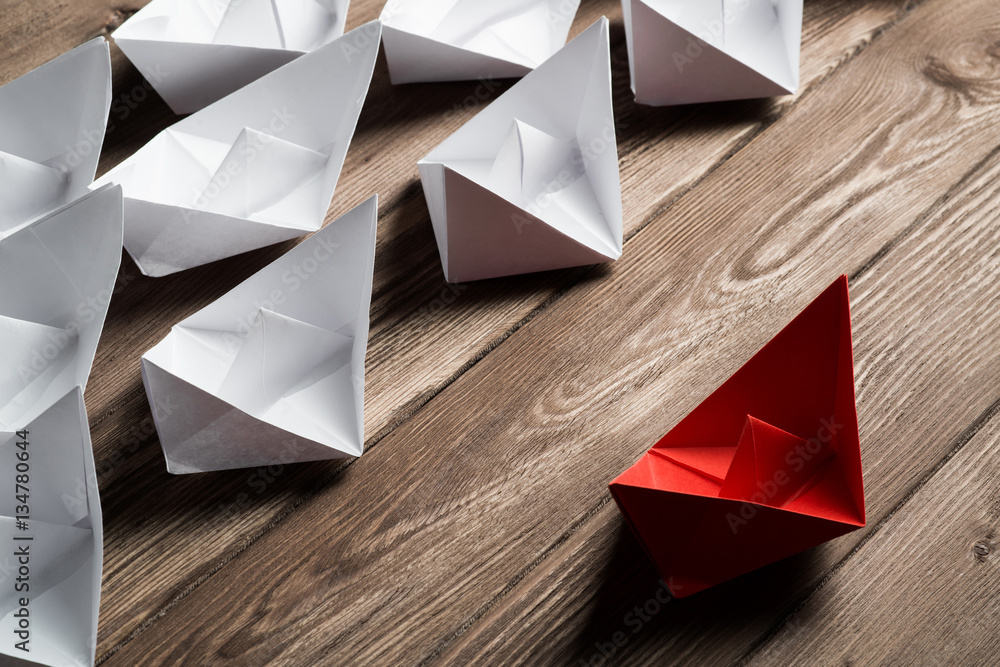 Business leadership concept with white and color paper boats on wooden table