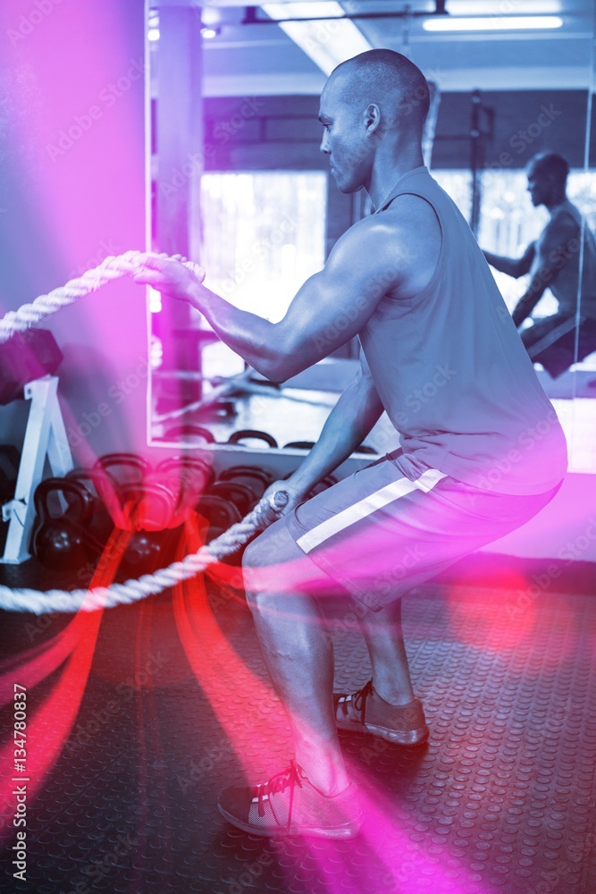 Side view of male athlete exercising with ropes