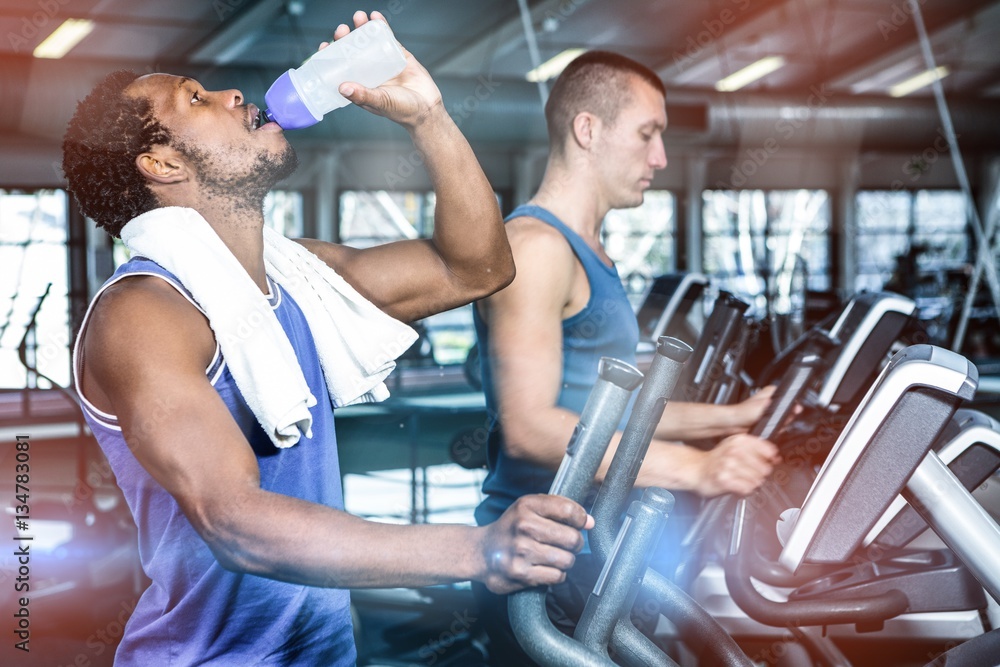 Man drinking water while using elliptical machine