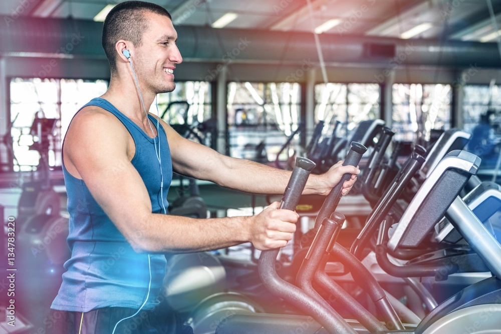 Smiling muscular man using elliptical machine