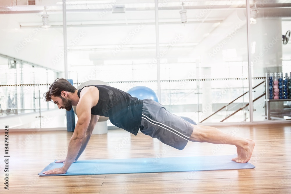 Side view of muscular man doing push up on mat