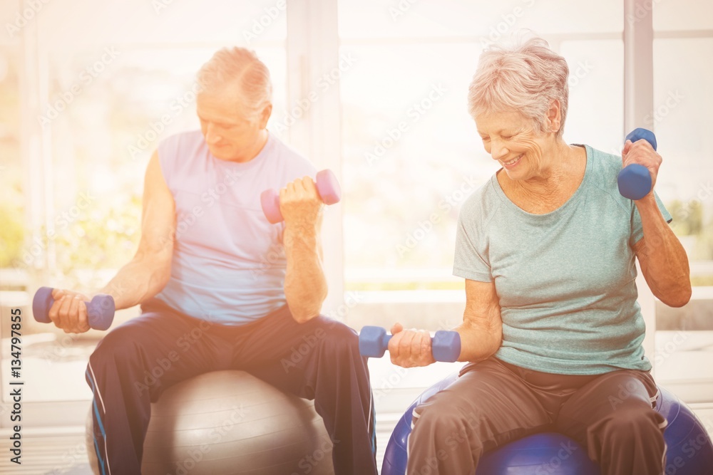 Smiling senior couple holding dumbbells while exercising