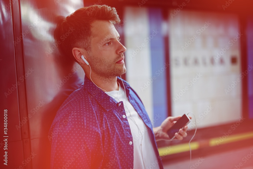 Man listening song while leaning on wall